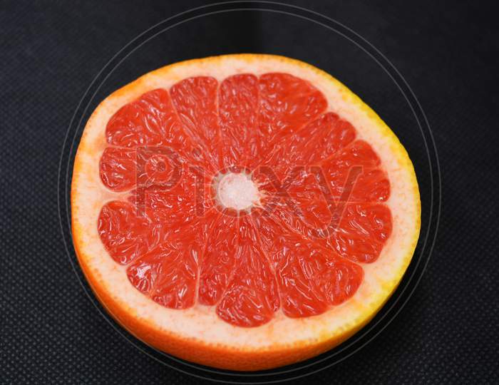 Halves of ripe juicy grapefruit, cut in half, set on a black fabric background. Delicious and healthy sweet and sour fruits for the human body and health.