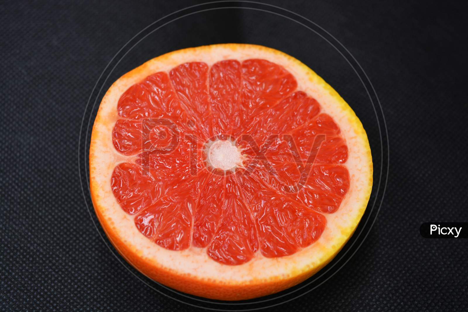 Halves of ripe juicy grapefruit, cut in half, set on a black fabric background. Delicious and healthy sweet and sour fruits for the human body and health.