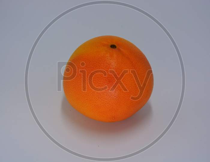 One big ripe delicious orange-red grapefruit arranged on a white plate. Delicious and healthy sweet and sour fruits for the human body and health.