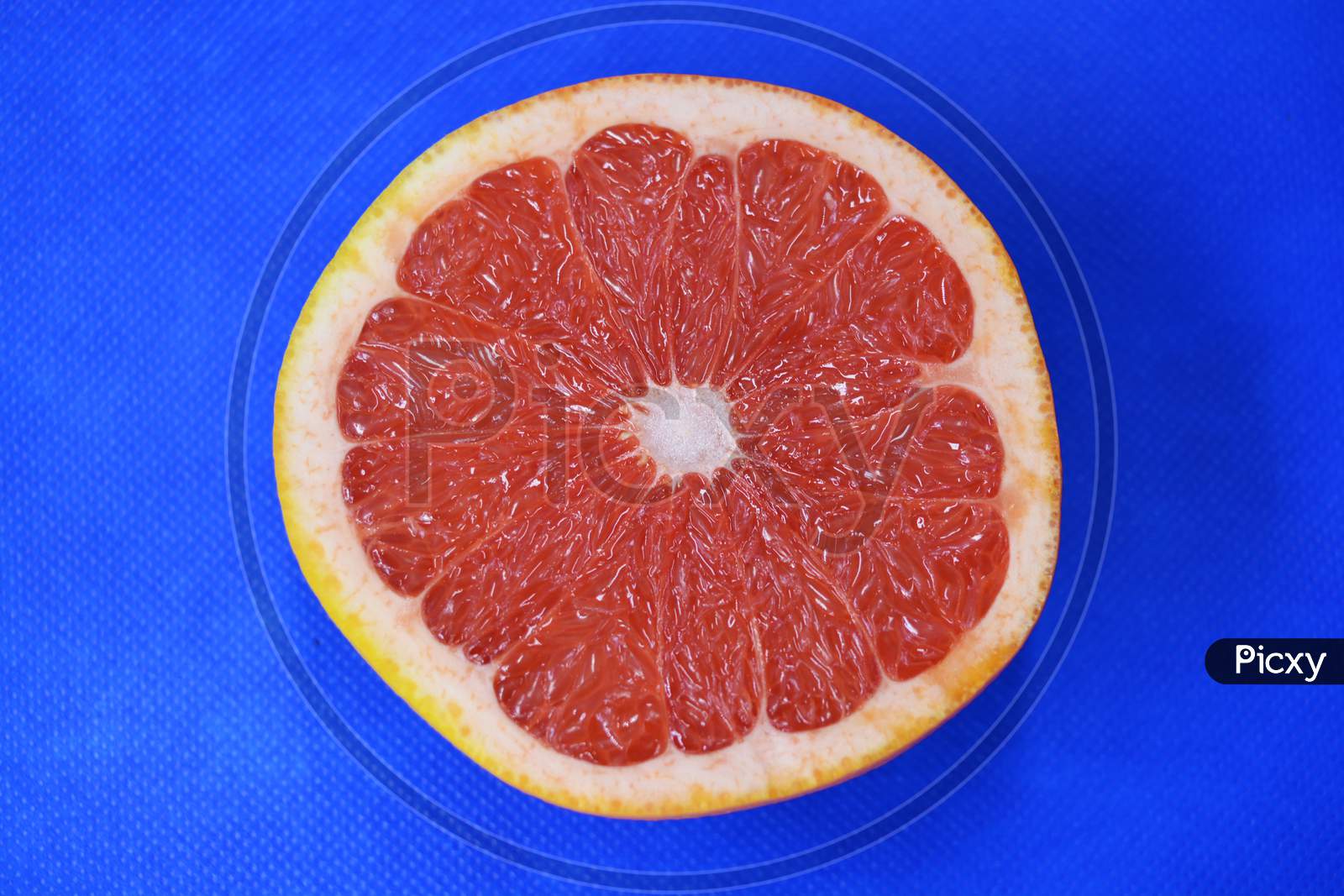 Halves of ripe juicy grapefruit, cut in half, set against a blue fabric background. Delicious and healthy sweet and sour fruits for the human body and health.