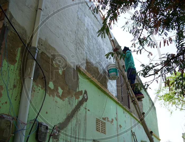 Male Painter Using Roller For Refurbishing Color Of Wall Outdoors. Indian Man Decorating The Walls.