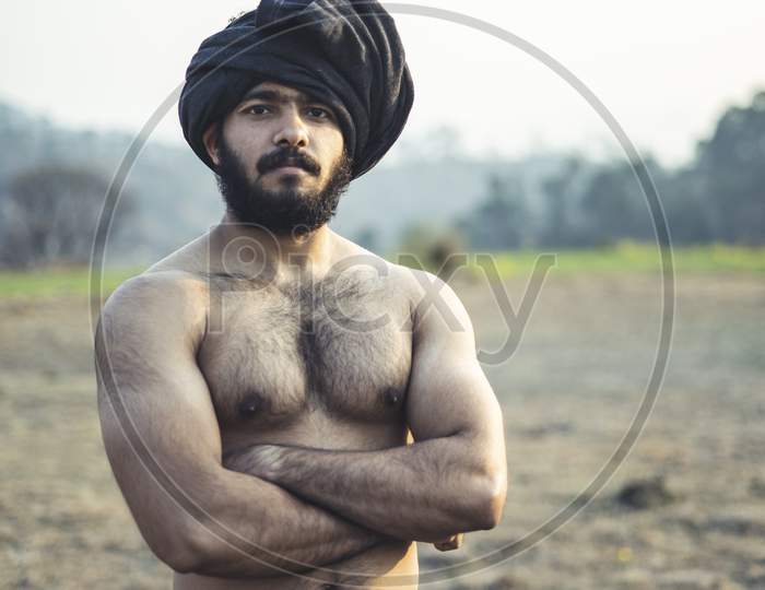 Young Indian Farmer With A Turban Standing On A Wasteland Field. Crops Not Growing Due To Shortage Of Rain And Water.