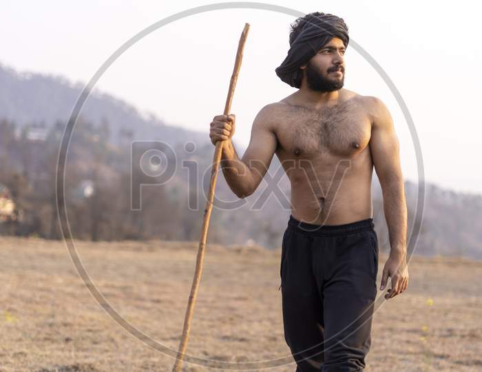 Crops Not Growing Due To Shortage Of Rain And Water.Young Indian Farmer With A Stick Walking In A Wasteland.
