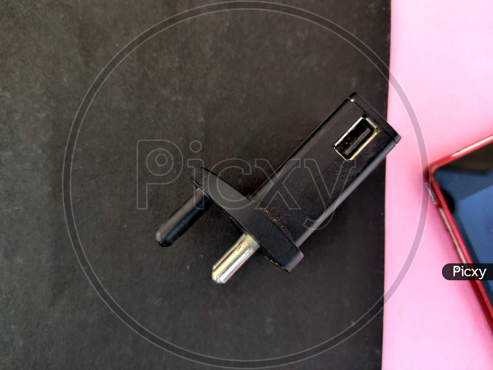 Top View Of Black Color Usb Charger With Red Color Mobile Phone Isolated On Pink And Black Background.