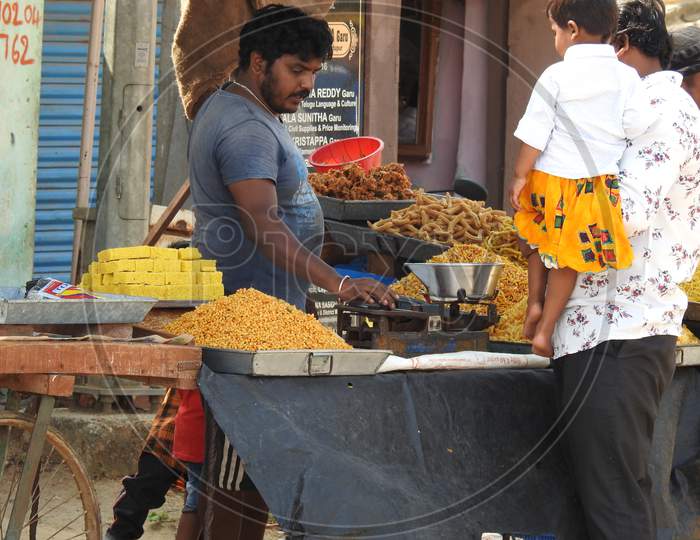 Closeup Of Roadside Sweets And Fried Food Selling In A Cart By Weighing In Traditional Weight Scale.