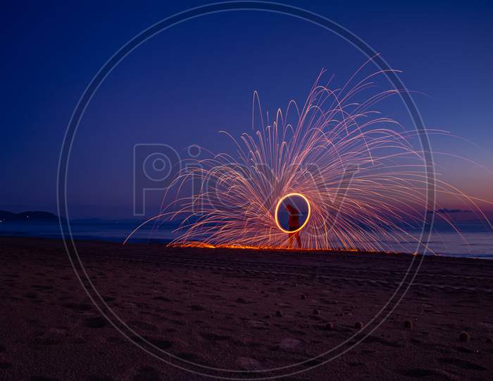 Silhouette Of Man On The Beach Making Sparks With Steel Wool. Long Exposure Light Painting Photography. Light Shapes On The Beach