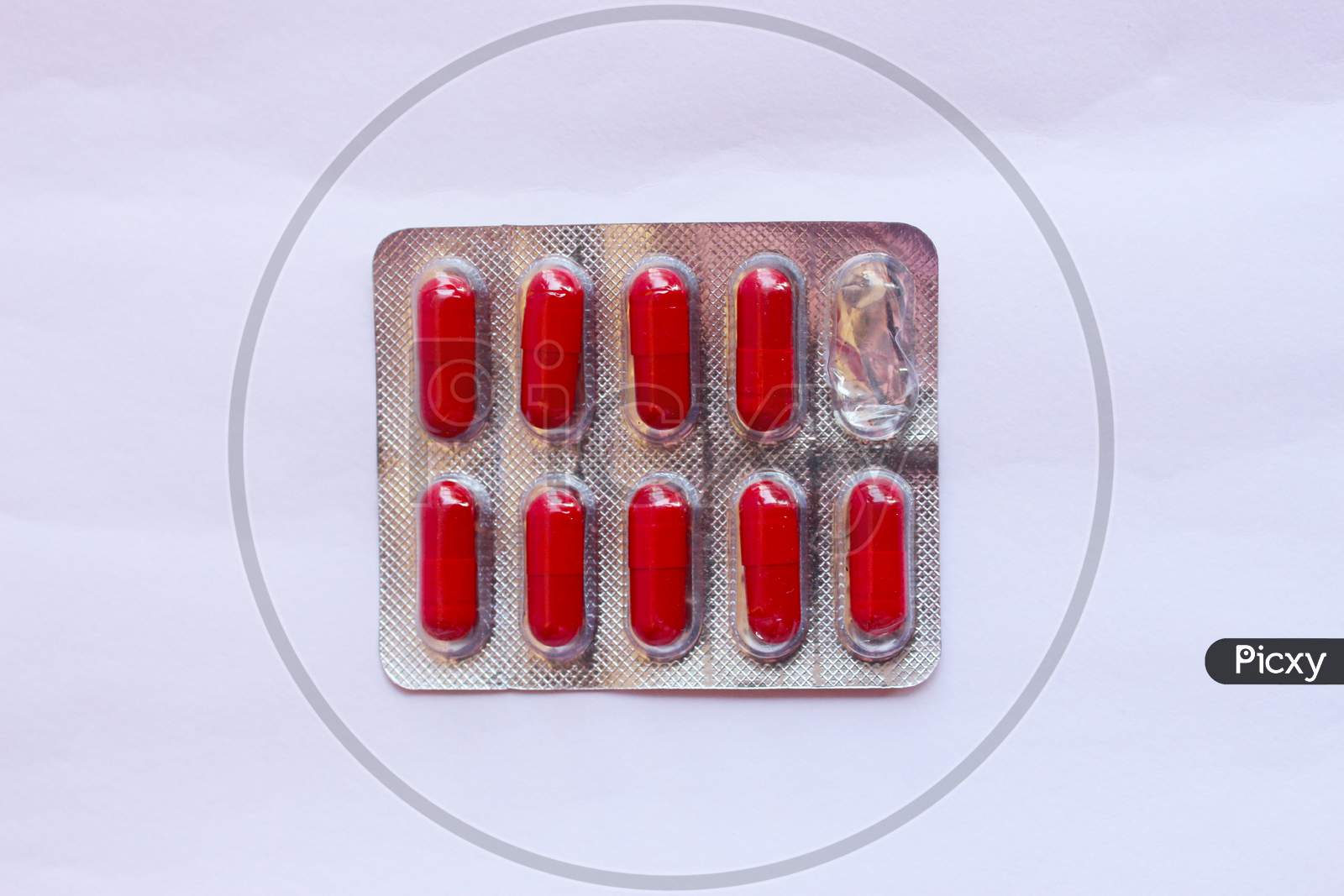 Blister Pack With Pharmaceutical Drug In The Form Of Red Capsules With One Used Capsule On A Light Colored Table, Top View