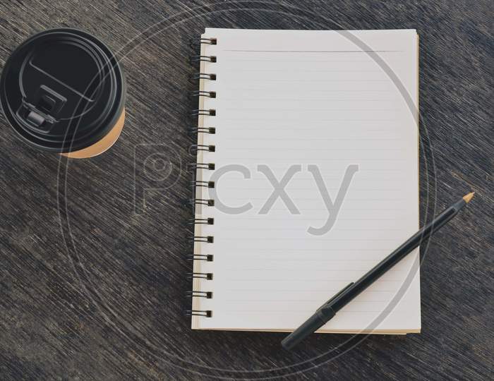 Notepad With Disposable Coffee Cup And Pen On Wooden Table. Blank For Text