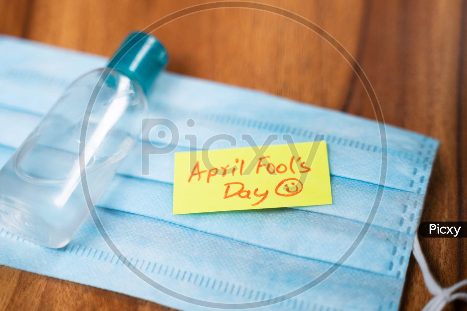 April Fools Day Sticky Note On Medical Face Mask With Hand Sanitizer Boottle On Table - Concept Of April Fools Day Celebrations During Coroanvirus Covid-19 Pandemic.