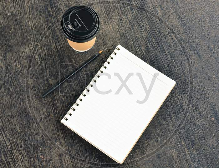 Notepad With Disposable Coffee Cup And Pen On Wooden Table. Blank For Text