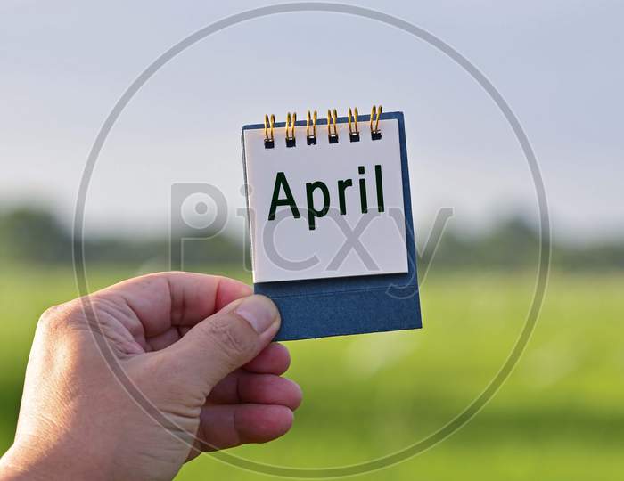 Hands Holding A Notepad With March Text Written And Blurred Green Background