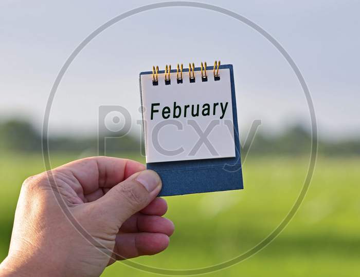 Hands Holding A Notepad With February Text Written And Blurred Green Background