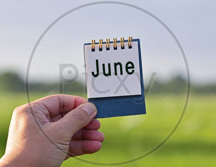 Hands Holding A Notepad With June Text Written And Blurred Green Background