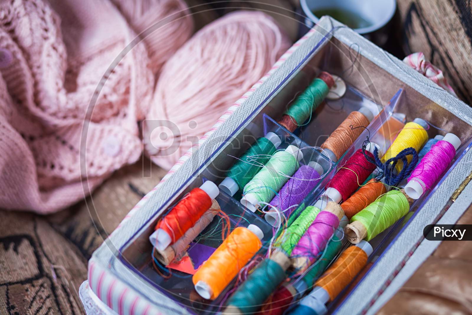 The Still Life Of A Tangle Of Pink Woolen Threads, An Unbound Pink Sweater And A Multitude Of Coils Of Thread Of Different Colors In The Box In Even Rows Lie On A Brown Vein, The Top View