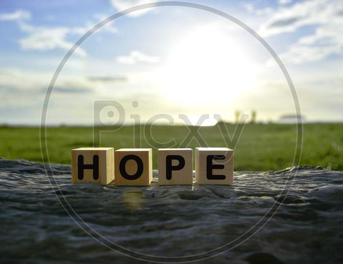 Hope Text On Wooden Cube Block On Old Tree Stump With Blurred Background Of Green Grass Ocean And Sunset