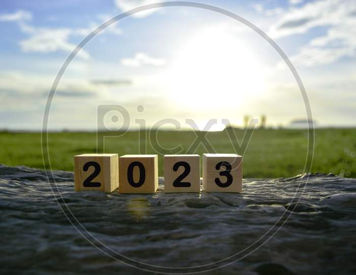 2023 Number On Wooden Cube Block On Old Tree Stump With Blurred Background Of Green Grass Ocean And Sunset