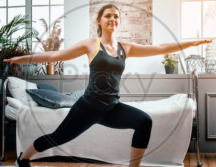 A Young Woman Goes In For Sports At Home, Online Workout From The Laptop. The Athlete Lunges   In The Bedroom, In The Background There Is A Bed, A Vase, A Carpet.