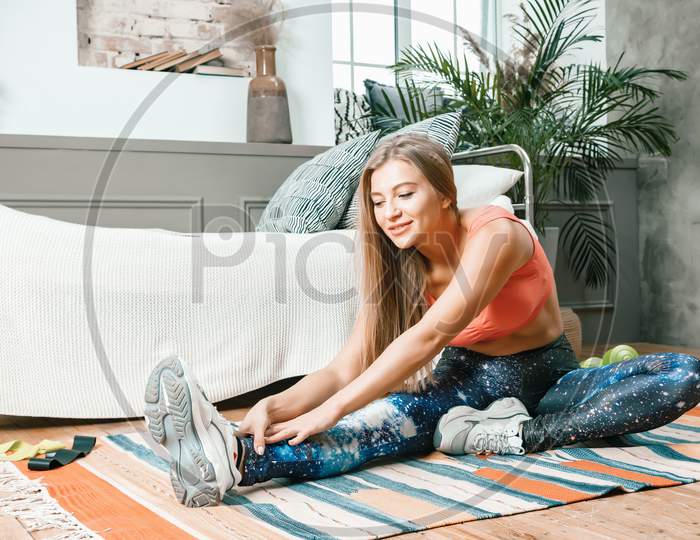 A Young Woman Goes In For Sports At Home, Online Workout . The Athlete  Stretching , Meditating, Sitting On A Floor  In The Bedroom