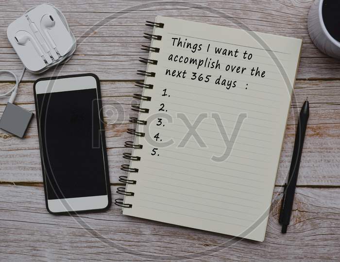 Text On Notepad With Cup Of Coffee, Smart Phone, Music Player And Pen On Wooden Desk