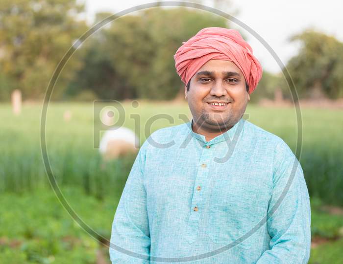 Portrait Of Young Happy Indian Farmer Wearing Traditional Kurta Outfit Standing In Agriculture Green Field. Closeup Looking At Camera.