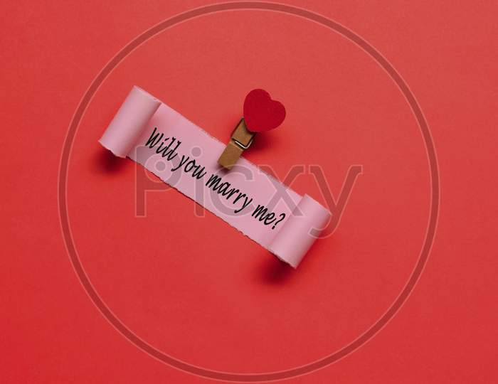 Will You Marry Me Label On Torn Paper With Red Paper Background. Valentine'S Day Concept