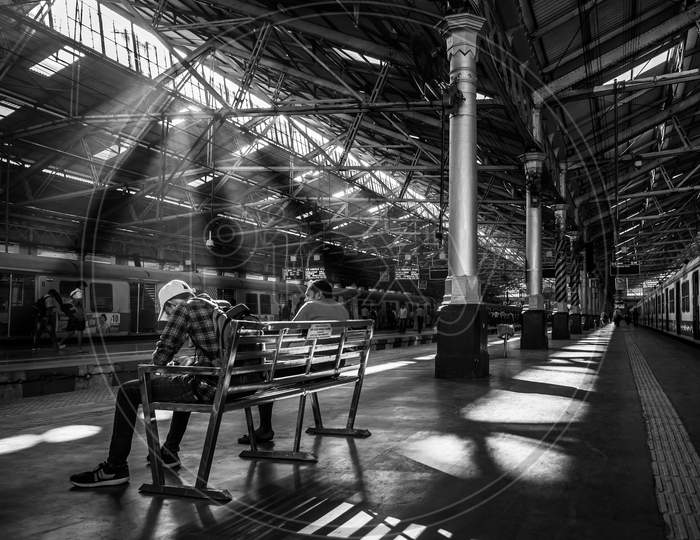 Unidentified Passengers Sitting On A Bench With Early Morning Sun Rays At Cst Station