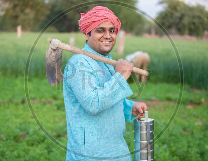 Portrait Of Happy Indian Male Farmer Holding Pretail Garden Spade / Shovel Or Agricultural Tool And Tiffing Box.