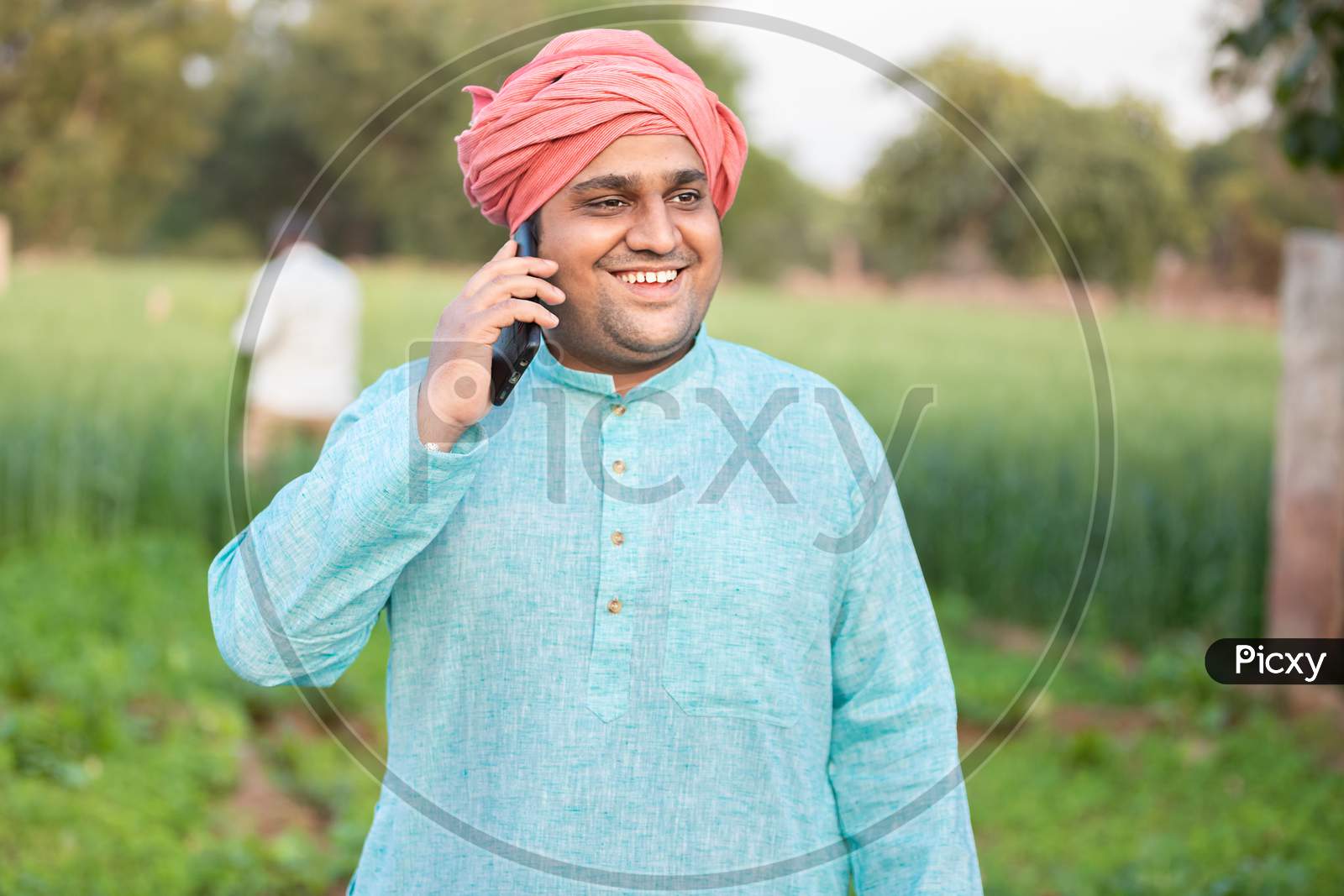 Young Happy Indian Farmer Worker Talking On Phone While Standing In Green Field, Agriculture And Technology Concept, Male Wearing Traditional Kurta Outfit, Copy Space To Write Text.