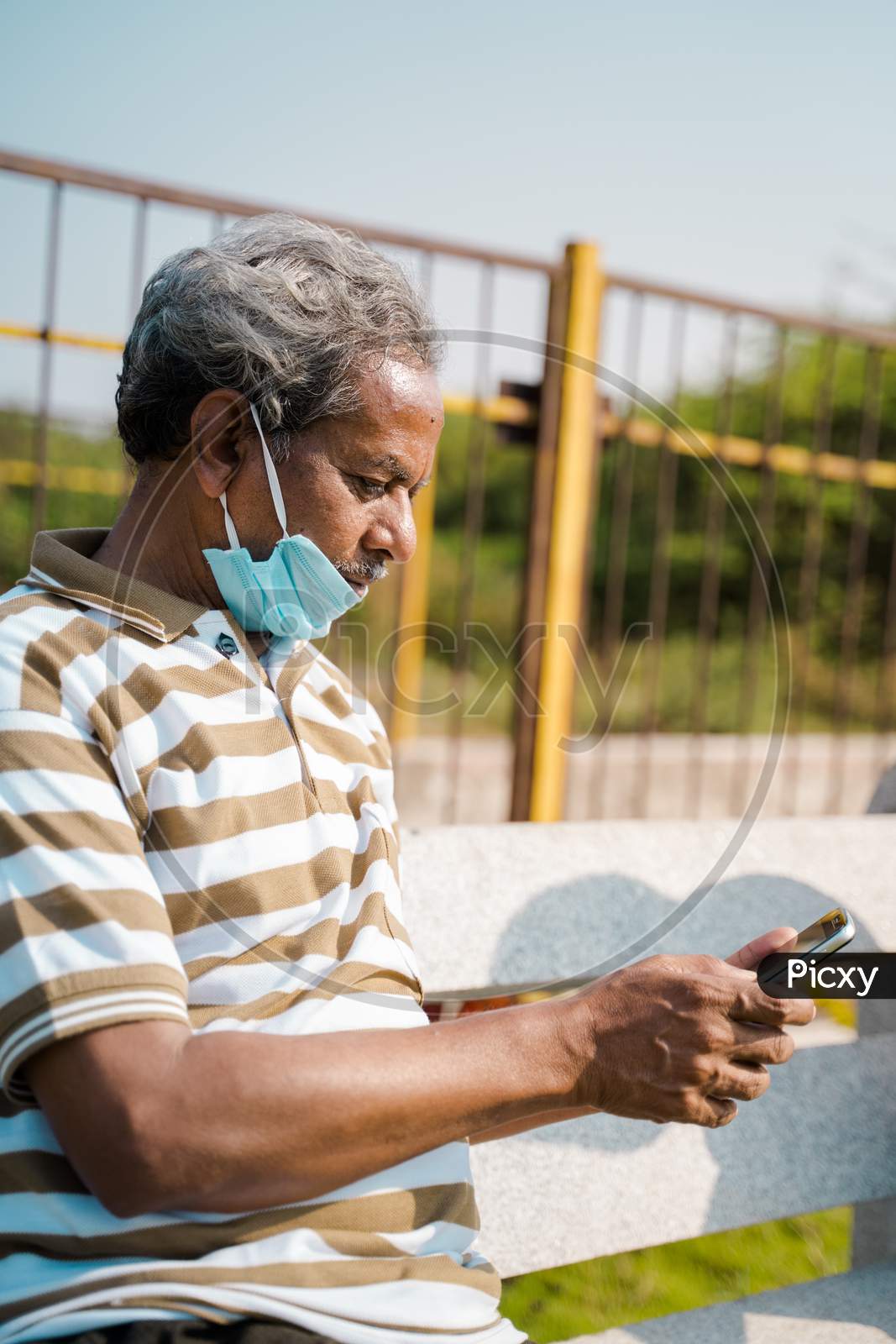 Senior Man With Medical Face Mask Below The Jaw Using Smartphone At Park - Concept Of Improper Mask Use Due To Coronavirus Covid-19 Pandemics.