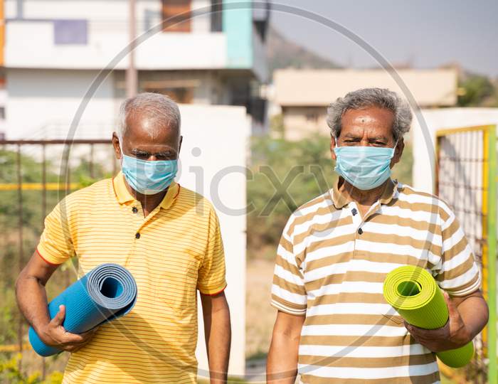 Two Senior People With Yoga Mat And Medical Face Mask In Park - Healthy Elderly Men With Fitness Mat Coming For Yoga During Coronavirus Covid-19 Pandemic