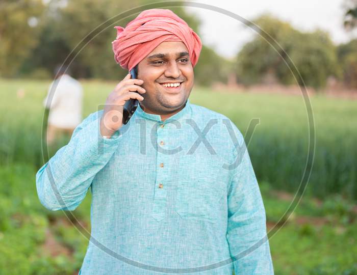 Young Happy Indian Farmer Worker Talking On Phone While Standing In Green Field, Agriculture And Technology Concept, Male Wearing Traditional Kurta Outfit, Copy Space To Write Text.