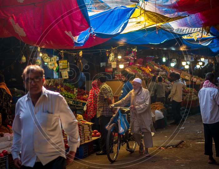 Muslim Old Age Man Wearing Traditional Islamic Cloths And Skull Cap Walking With Bicycle In A Fruit Market In South Mumbai