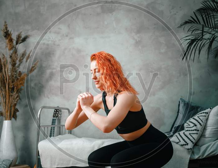 A Strong And Beautiful Sports Fitness Girl In Sportswear Doing Squats In Her Bright And Airy Bedroom With A Minimalistic Interior.
