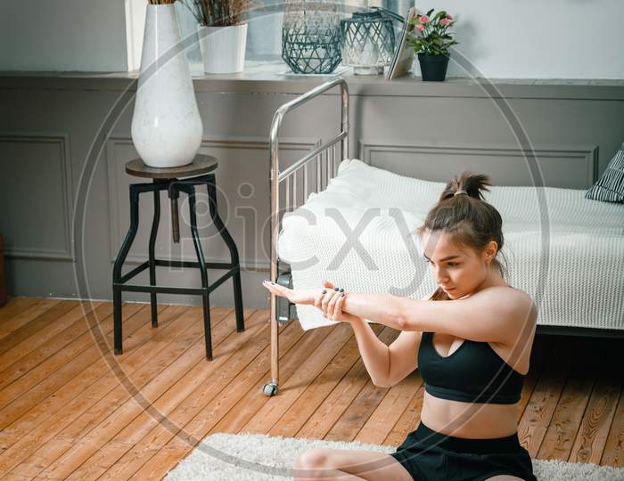 A Strong And Beautiful Sports Fitness Girl In Sportswear Meditates In Lotus Position, Resting On The Floor At Home In Her Bright And Airy Bedroom With A Minimalistic Interior.