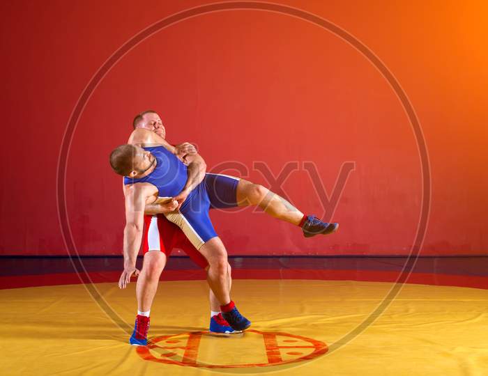 Premium Photo  Two strong wrestlers in blue and red wrestling tights are  making a hip throw on a yellow wrestling carpet in the gym.