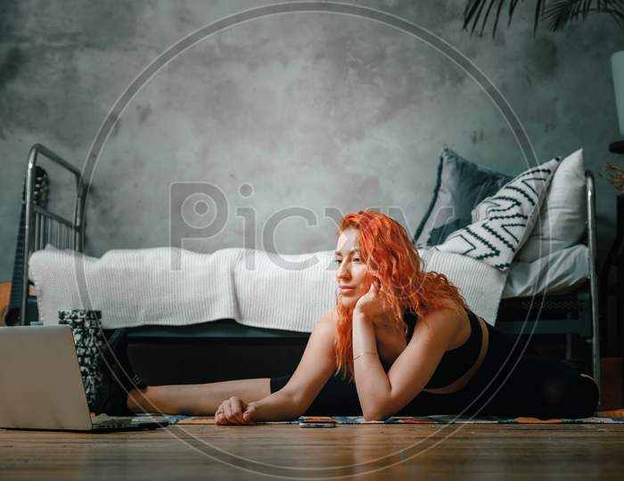 The Beauty Woman Goes In For Sports At Home. Cheerful Sporty Woman With Red Hair Stretches To The Leg   In The Bedroom