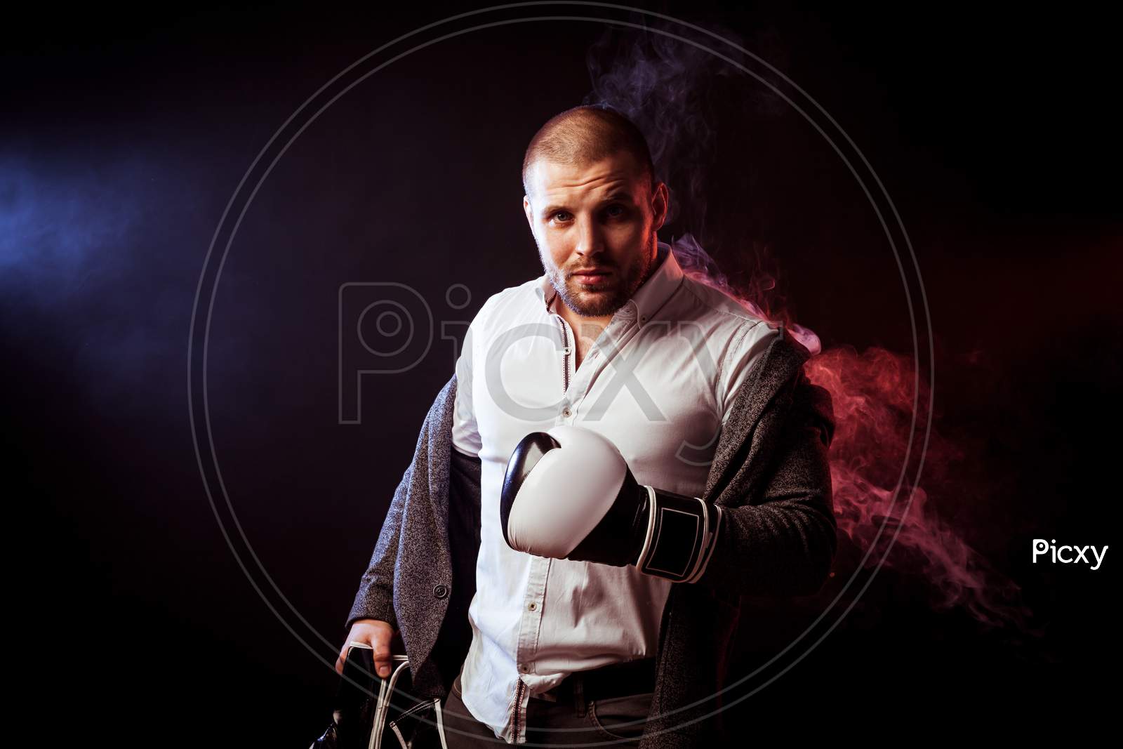 Young Handsome Man Businessman In White Shirt, Gray Suit, White And Black Gloves  Took Off His Jacket And Looked Inquiringly  Against Red  And Blue Smoke From A Vape  On Black Isolated