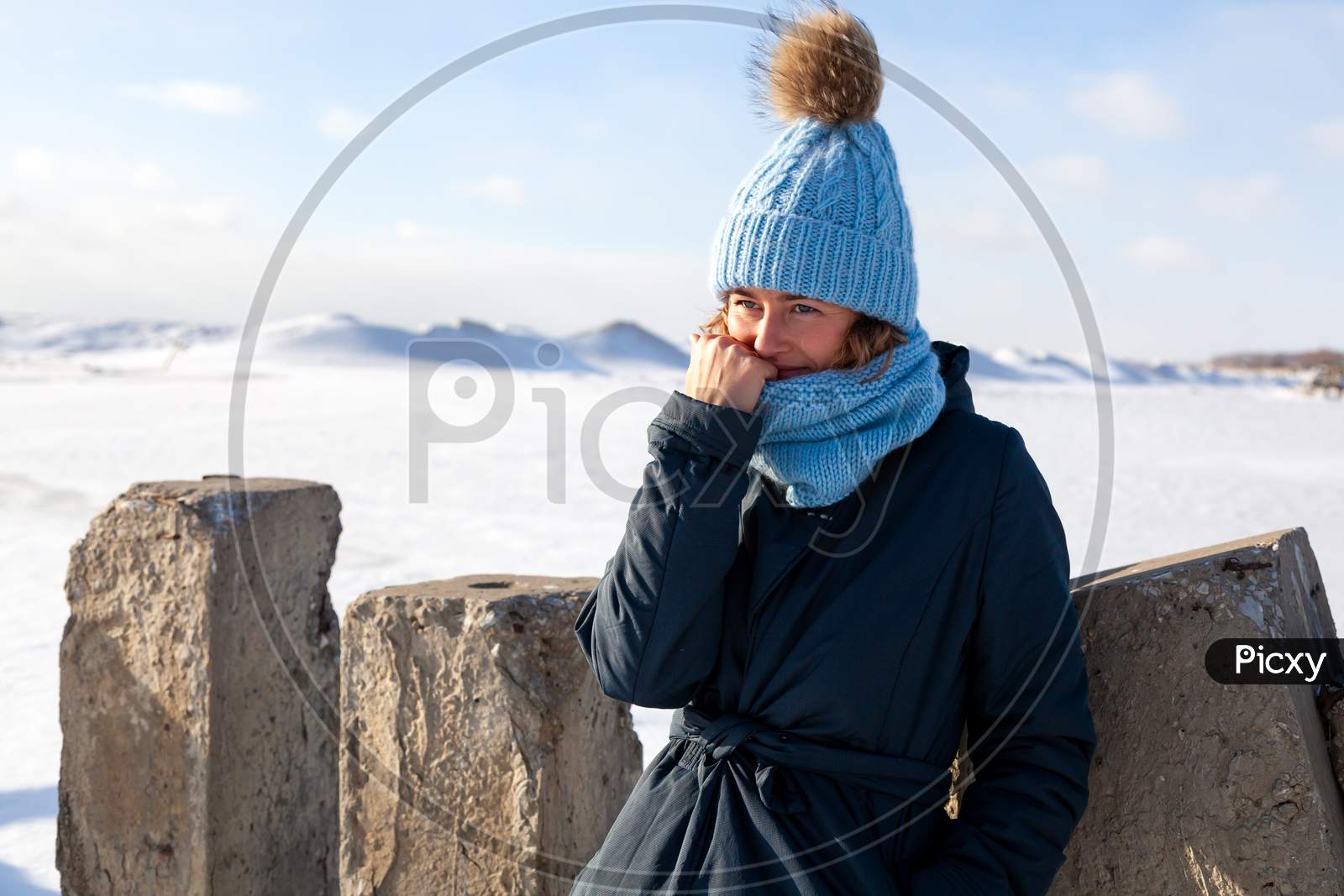 Portrait Beauty Woman Model On Winter Background. Beautiful Modern Urban Young Woman Wearing Blue Knitting Hat  Basks In Cold Weather On The Background Of The Frozen Sea