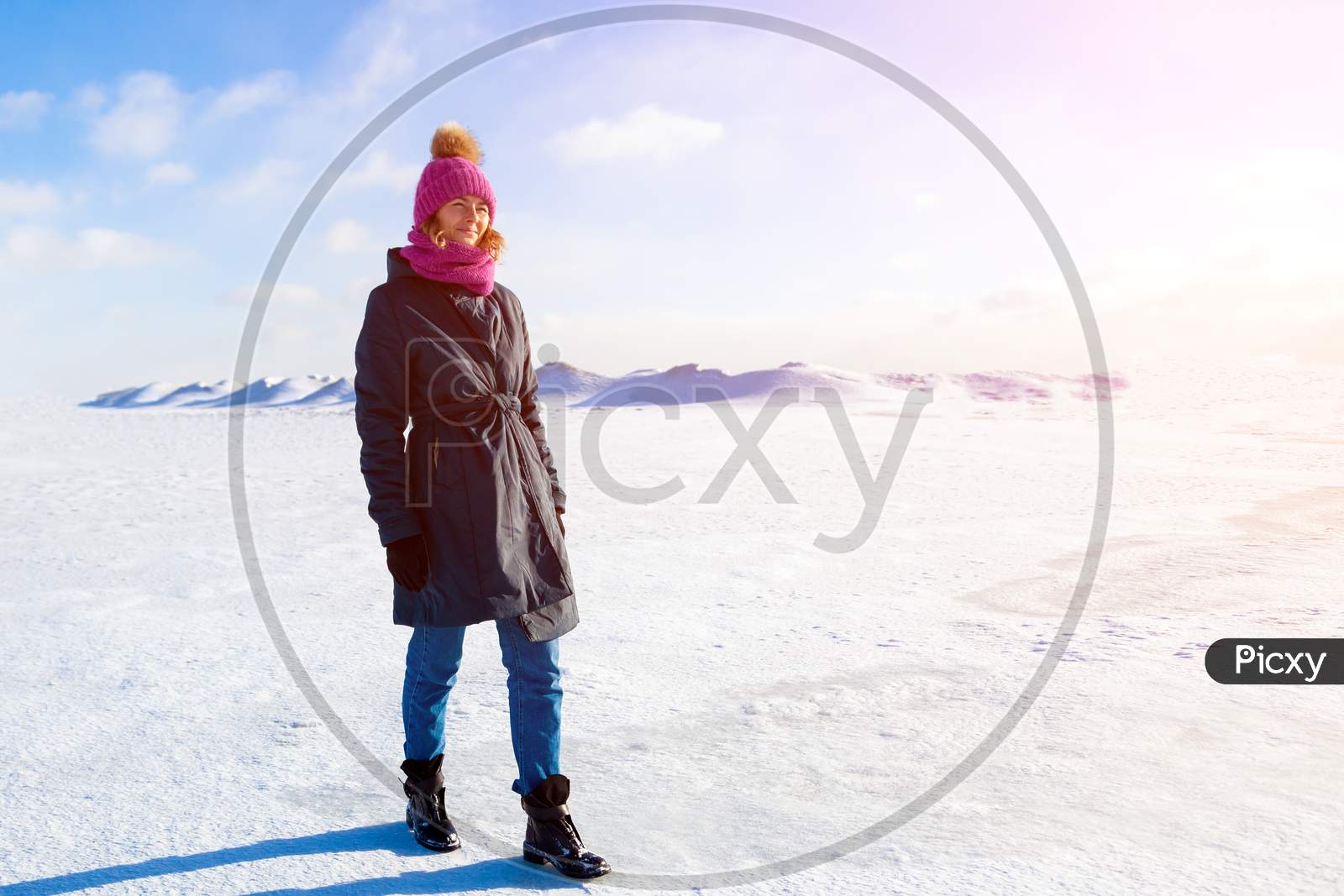 A Young Woman  In Warm Coat And  Hat Enjoys  Winter Nature, Walking And Chat On  Snow In  Frozen Sunny Day In The Background Of A Snow Mountains, Blue Sky And Sunny