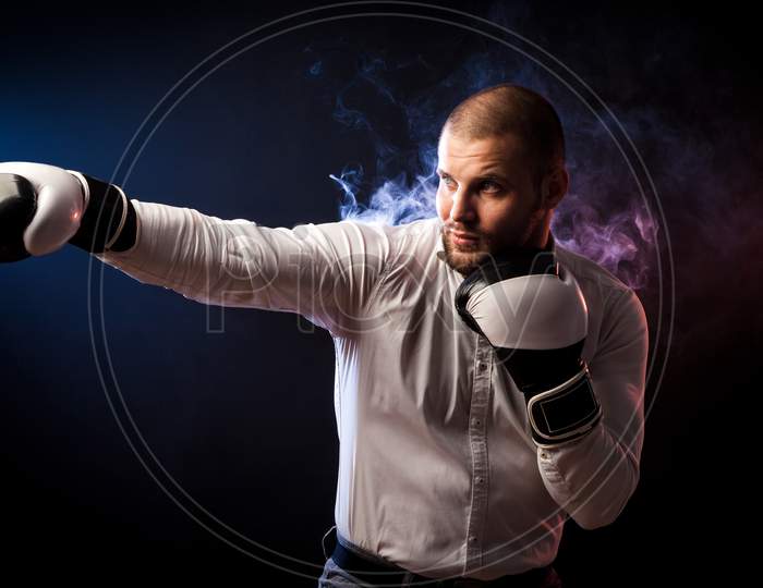 Handsome Young Man Businessman In White Shirt And Black And White Boxing Gloves Boxing In Front Of Red And Blue Smoke From A Wipe On A Black Isolated Background