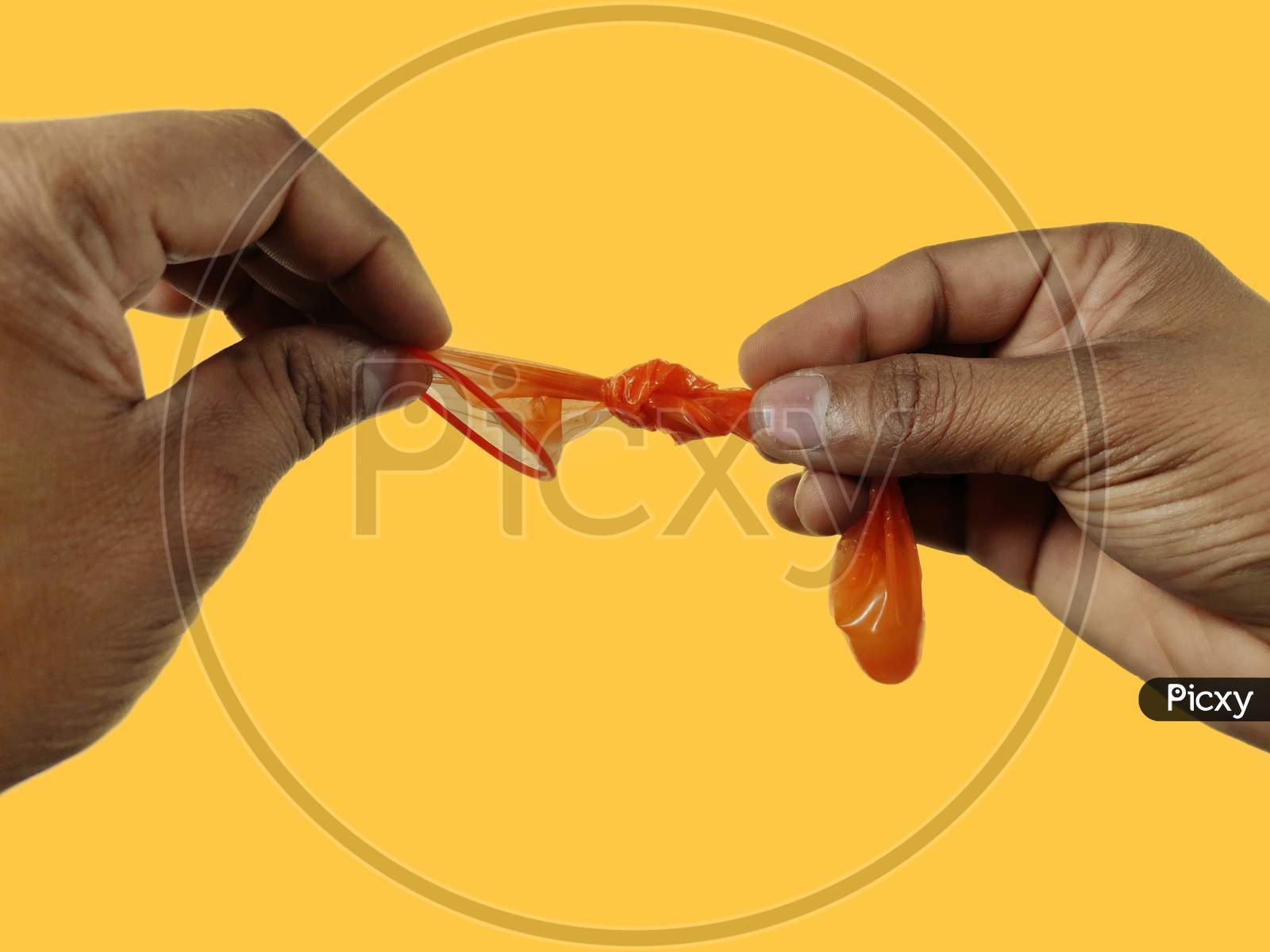 Condom end tie by hands  to prevent sperms fallout on yellow background with space for text.