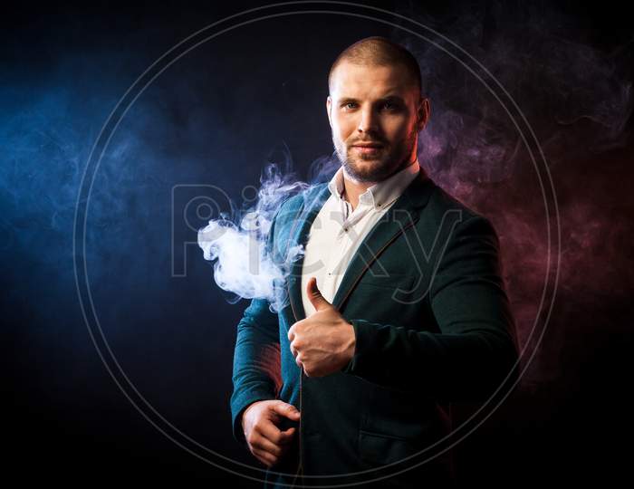 Young Handsome Businessman Man In White Shirt And Green Jacket Smiling And Showing Thumb Up Opposite Red And Blue Smoke From Wipe On Black Isolated Background