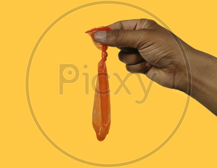 Man hand holding Orange Used condom against yellow background , space for text