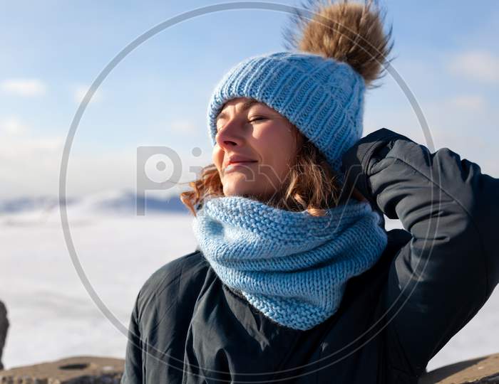 Portrait Beauty Woman Model On Winter Background. Beautiful Modern  Young Woman Wearing Blue Knitting Hat  Warm Hands, Smile, Look At Camera On A Walk On The Frozen Sea In Winter