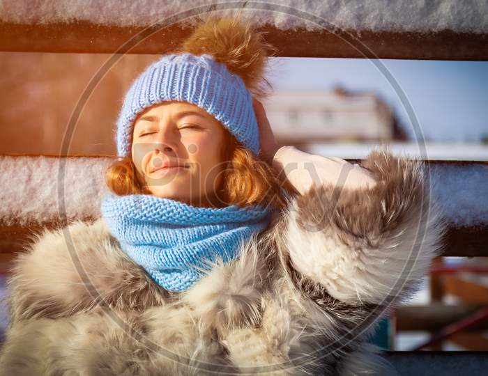 Portrait Beauty Woman Model On Winter Background. Beautiful Modern  Young Woman Wearing Blue Knitting Hat Enjoy, Smile On A Walk On The Frozen Village In Winter