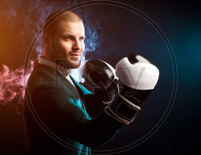 Young Handsome Businessman Man In White Shirt, Green Jacket, Black And White Boxing Gloves Smiling And Ready To Box Against The Red And Blue Smoke From The Paper On A Black Isolated Background