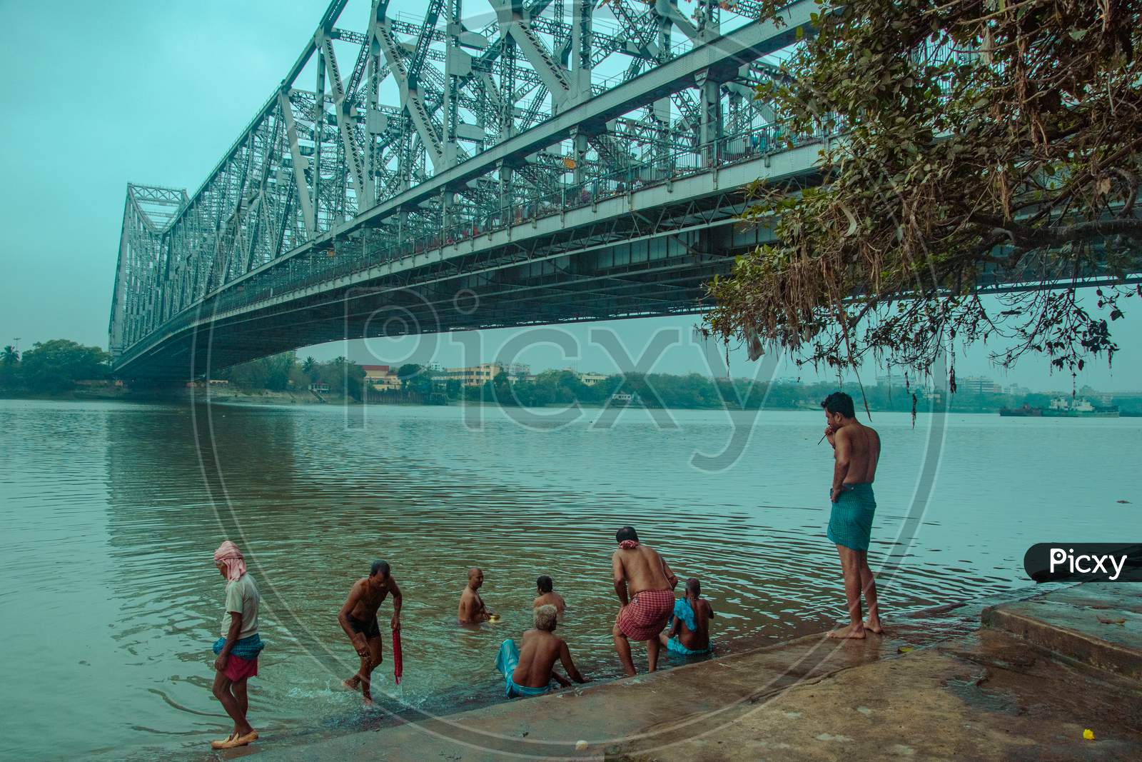 PEOPLE BATHING IN HOOGHLY RIVER UNDER HOWRAH BRIDGE, KOLKATA, WEST BENGAL.