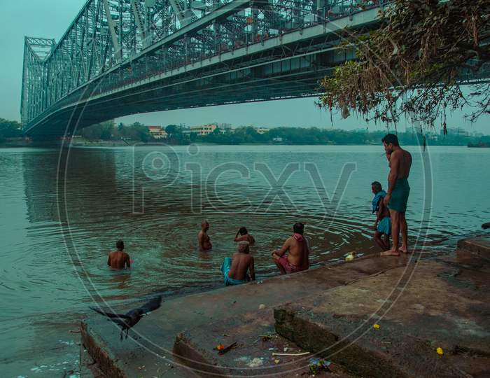 PEOPLE BATHING IN HOOGHLY RIVER UNDER HOWRAH BRIDGE, KOLKATA, WEST BENGAL.