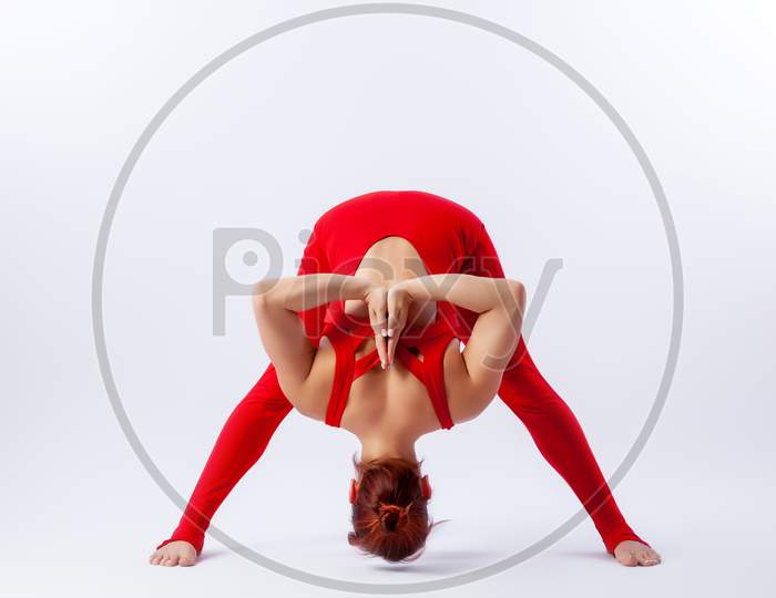 Beautiful Slim Woman In Sports Overalls  Doing Yoga, Standing In An Asana Balancing Pose - Prasarita Padotanasana  On White  Isolated Background. The Concept Of Sports And Meditation. Training For Stretching And Yoga