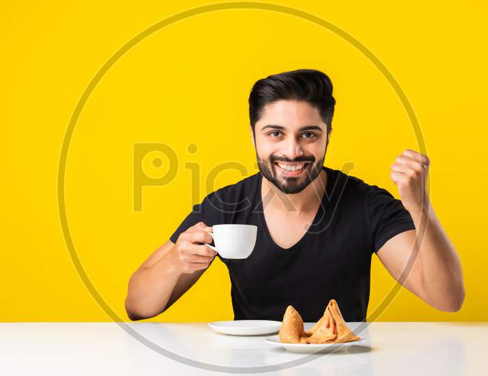Indian Asian Handsome Young Man Drinks Tea Or Coffee From White Cup Against Yellow Background